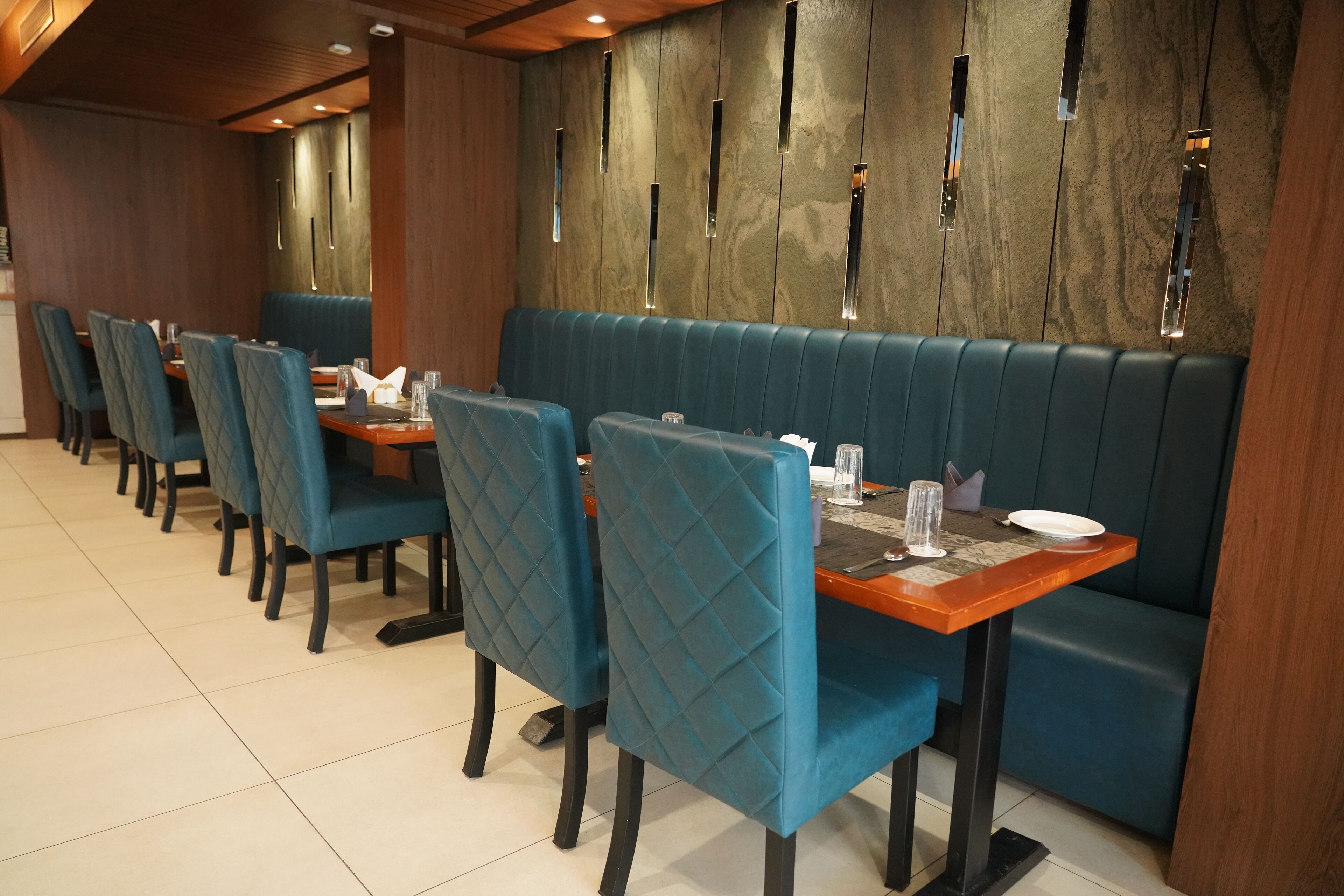 A restaurant with blue upholstered booths and chairs, wooden tables, and a modern wall design with vertical light fixtures.