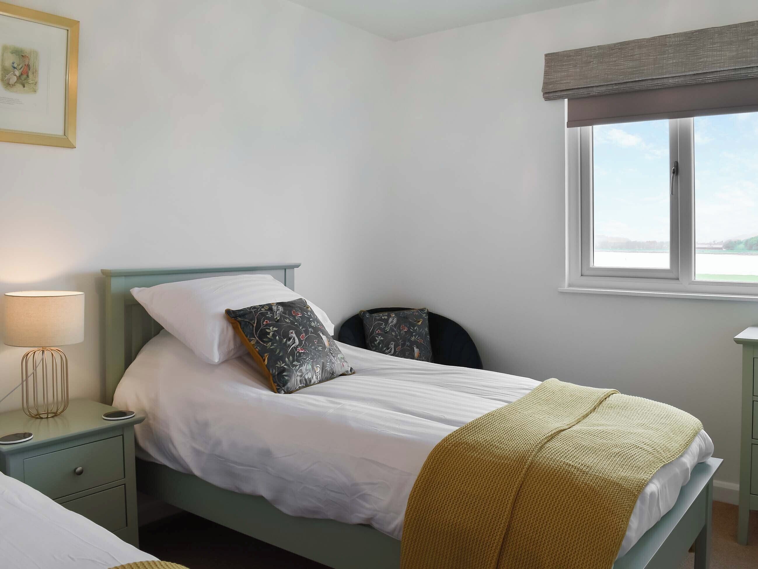 Une chambre avec un lit simple, une table de chevet avec une lampe, une chaise et une fenêtre donnant sur un beau paysage.