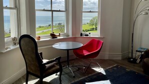 Ein Zimmer mit Meerblick, ein roter Sessel, ein Tisch und eine Stehlampe.