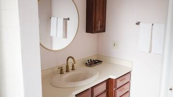 A bathroom with a sink, mirror, vanity, and wooden cabinets.