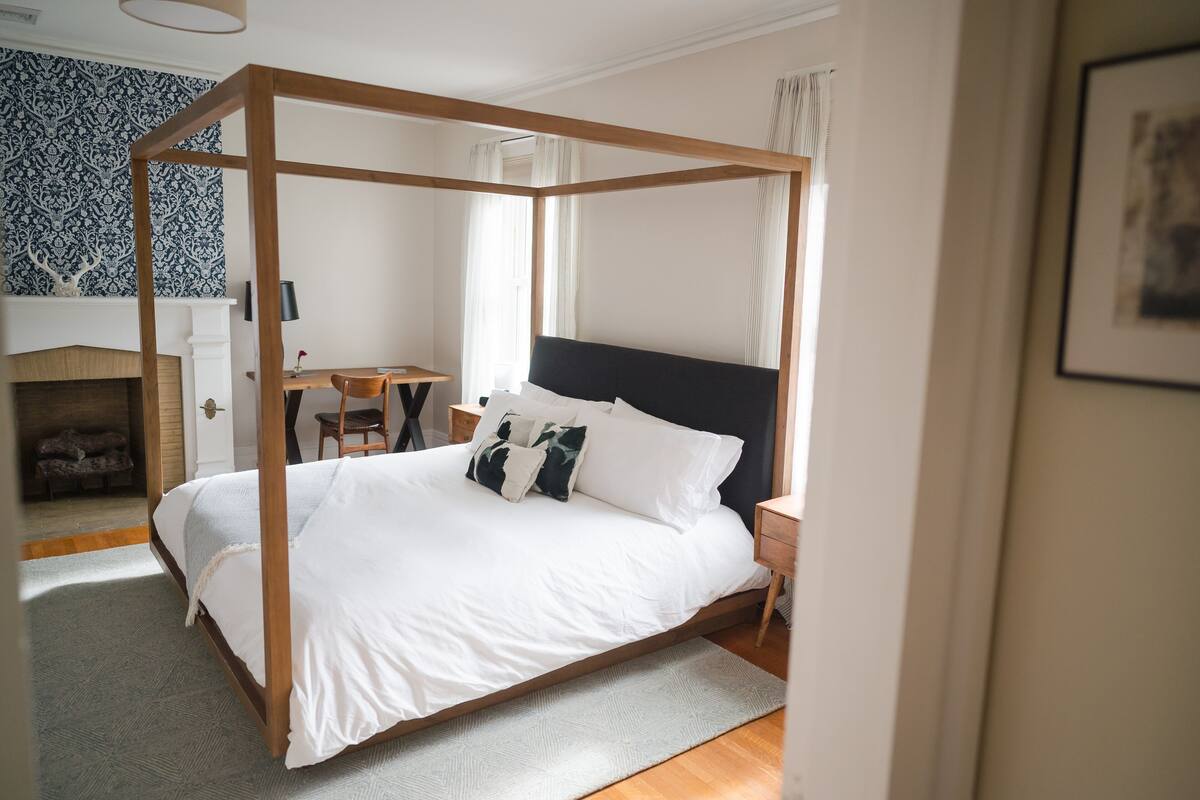 A four-poster bed with white linens, a wooden headboard, and a bedside table with a lamp.