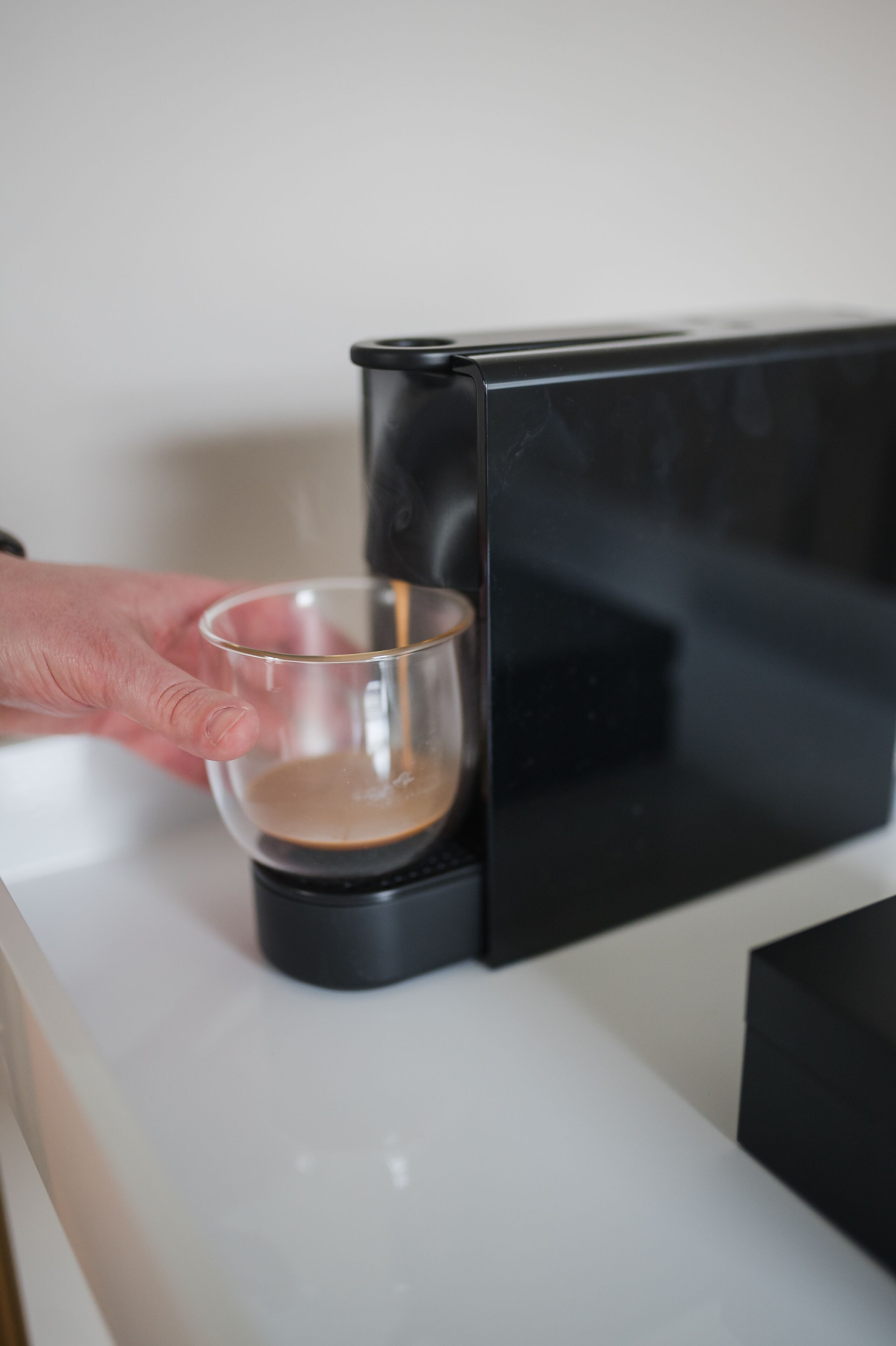 Une main tenant un verre près d’une machine à café.