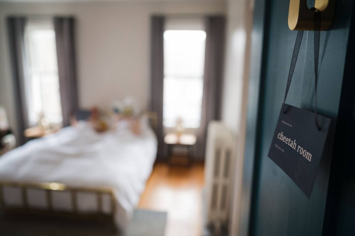 A bedroom with a bed, a nightstand, and a window. There is a sign on the wall that reads "cheetah room".