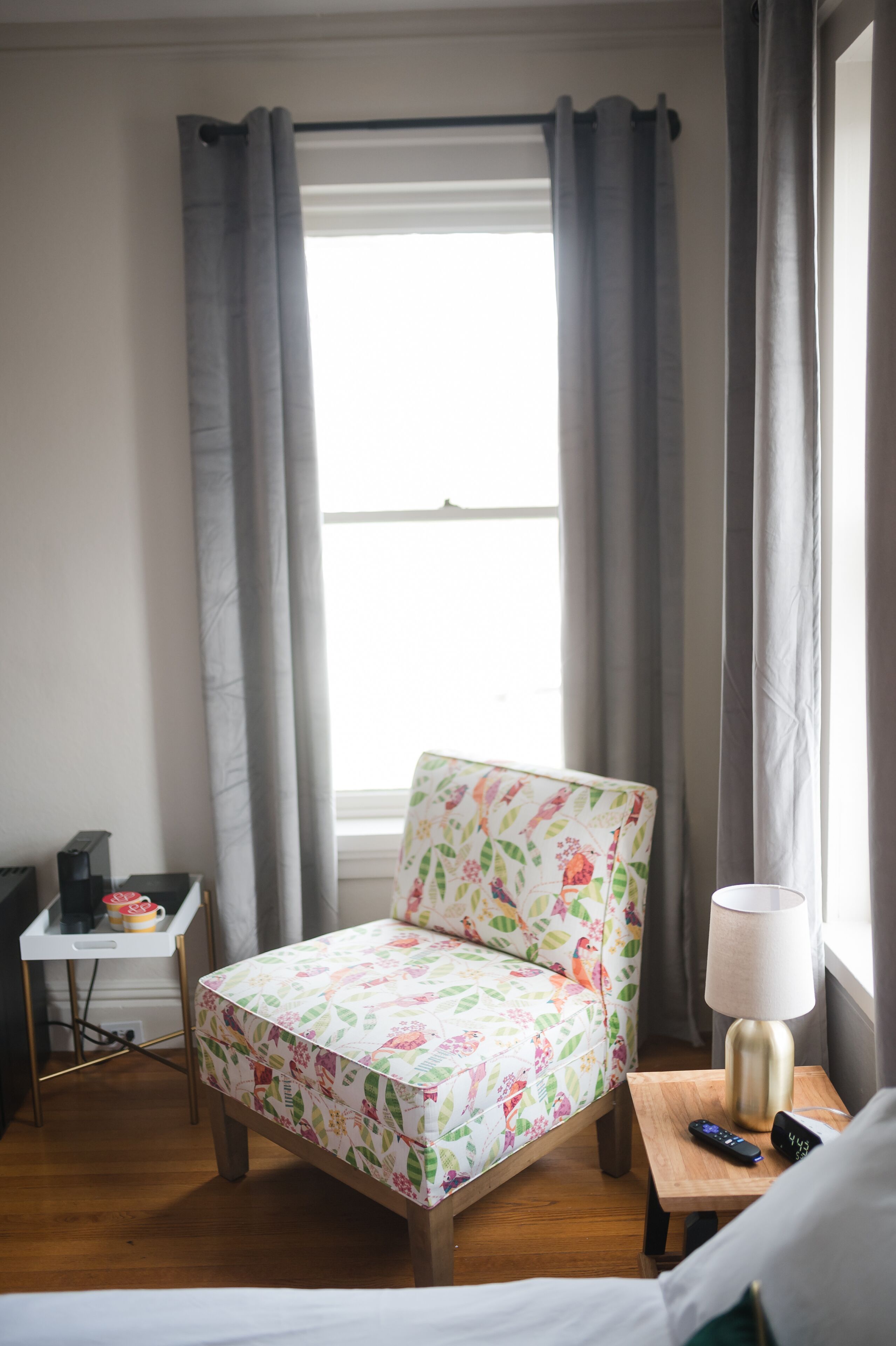 Una habitación pequeña y acogedora con una silla de madera, una mesita con una lámpara y una cama.