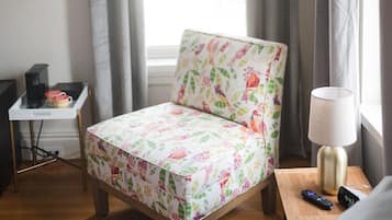 Una habitación pequeña y acogedora con una silla de madera, una mesita con una lámpara y una cama.