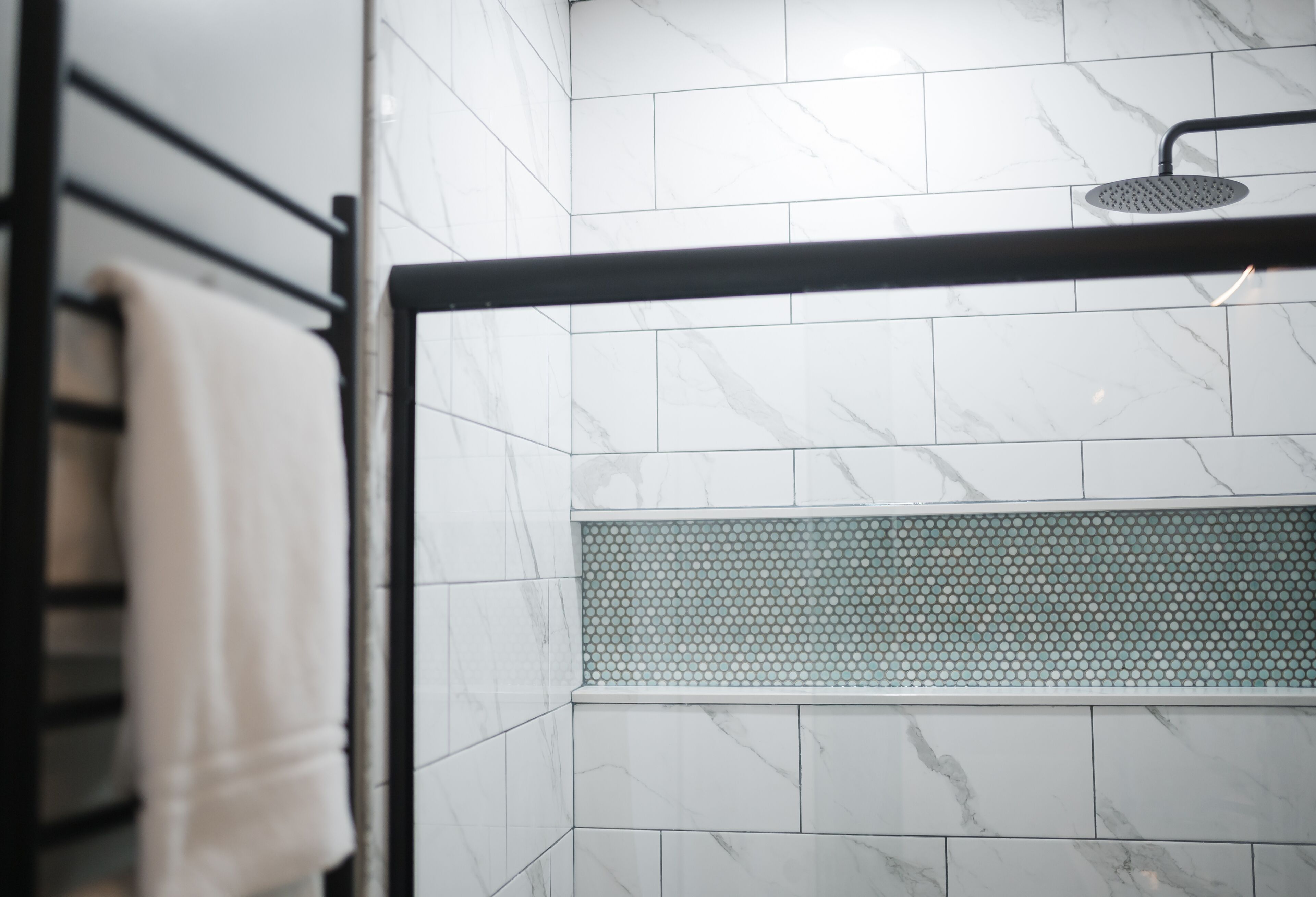 A bathroom with white marble tiles, a shower area with a black frame, and a towel rack.