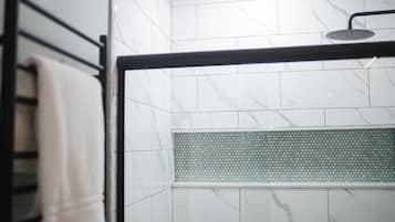 A bathroom with white marble tiles, a shower area with a black frame, and a towel rack.