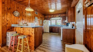 A wooden cabin kitchen with a central island, wooden cabinets, a refrigerator, and a clock. - Virginia's Beach - Cozy Oceanfront Beach Cottage! (Surf City)