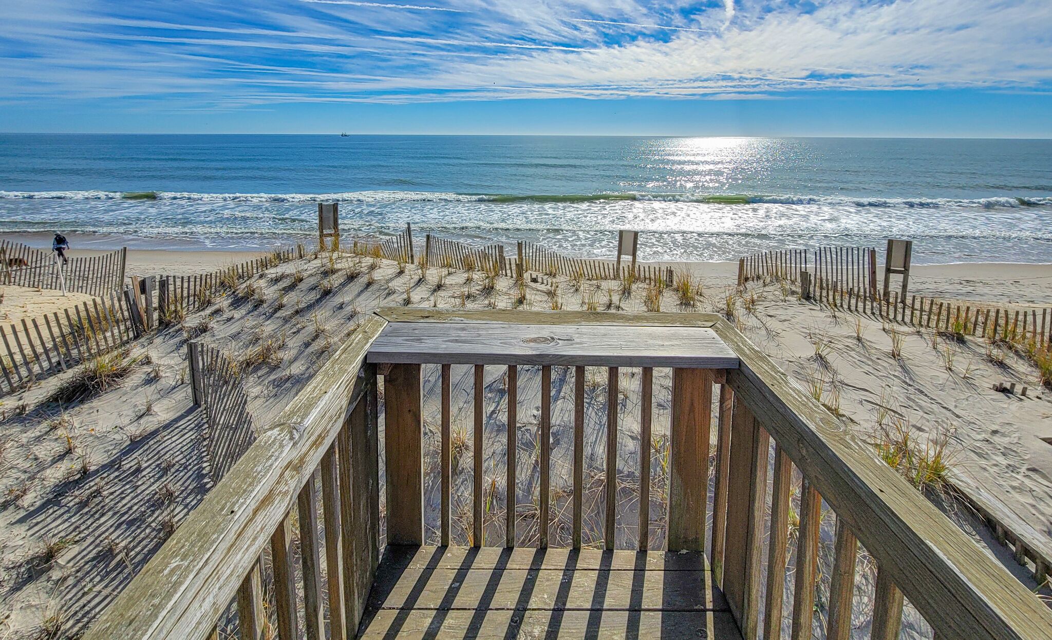 A wooden boardwalk leading to a beach with a clear view of the ocean and a ship in the distance.