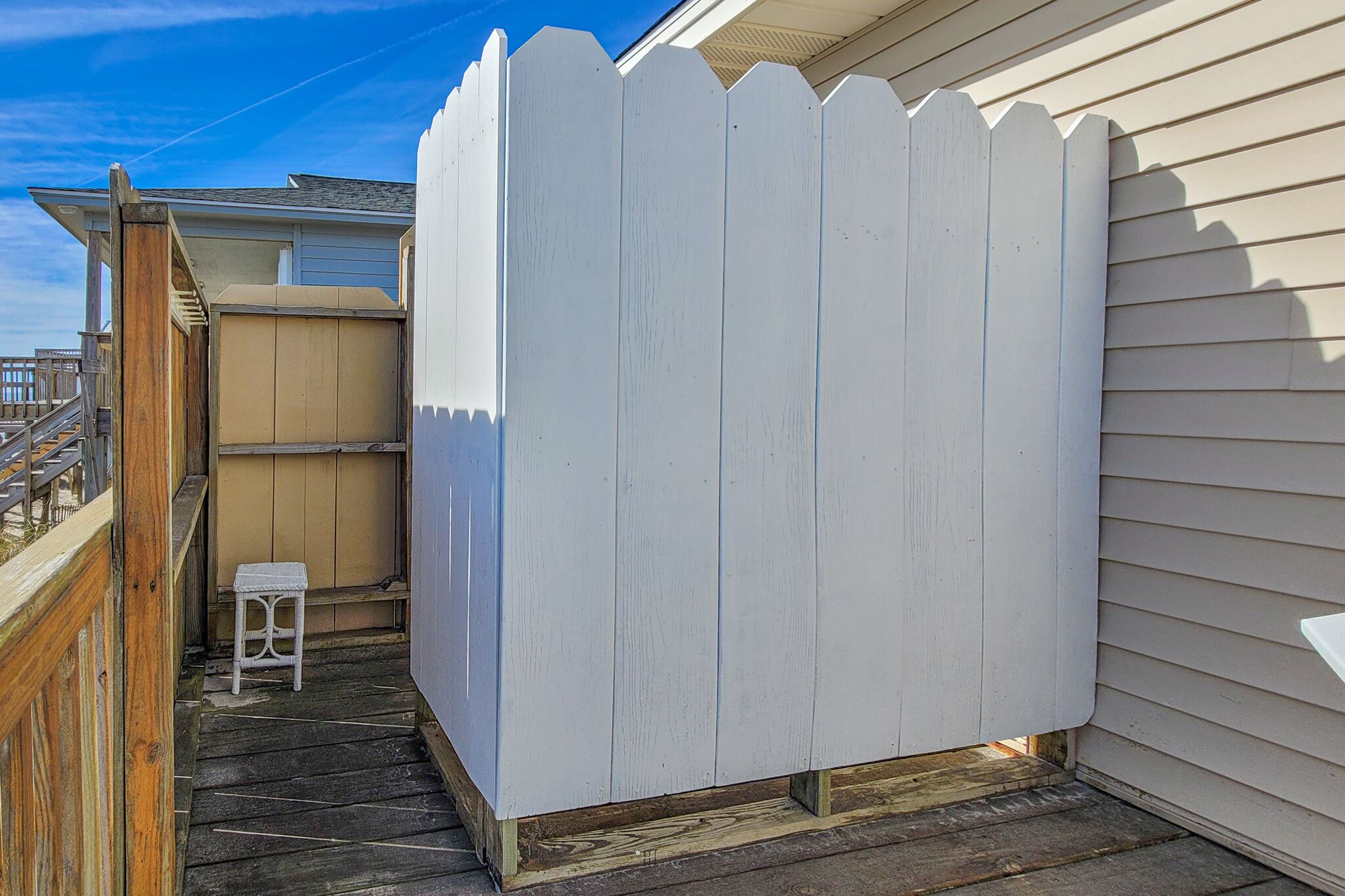A wooden deck with a white picket fence, a small white stool, and a wooden bench.