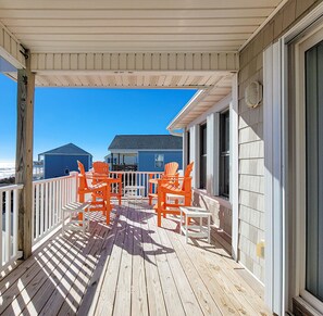 A wooden deck with white railings and orange Adirondack chairs.