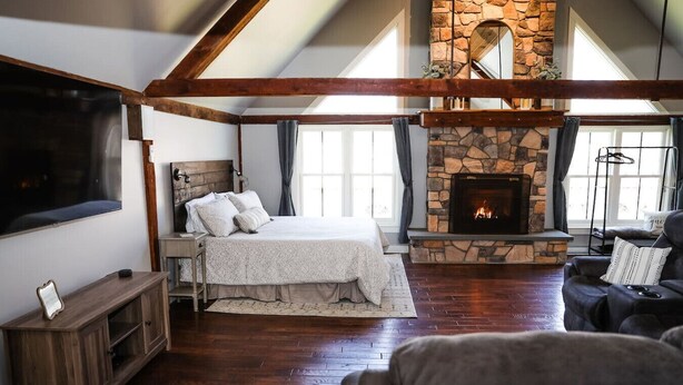 A bedroom with a stone fireplace, a large bed, a TV, and a wooden floor.