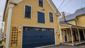 A two-story yellow house with a dark blue garage door, a covered porch, and a chimney.