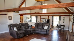 A spacious living room with a sectional sofa, wooden beams, a dining area, and a kitchen in the background.