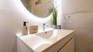 A bathroom with a white sink, a mirror, a plant, and two soap dispensers.