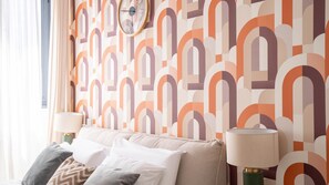 A room with a patterned wallpaper, a sofa with cushions, two lamps, and a clock on the wall.