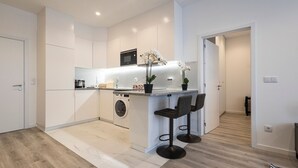 A modern kitchen with a central island, a washing machine, and a microwave. There are two bar stools and a potted orchid on the island. - CasaBela 5 Star Matosinhos Sun&Beach by LovelyStay (Matosinhos)