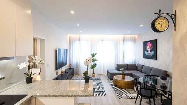 A modern living room with a sofa, coffee table, and TV. There is a clock on the wall and a plant on the floor. - CasaBela 5 Star Matosinhos Sun&Beach by LovelyStay (Matosinhos)