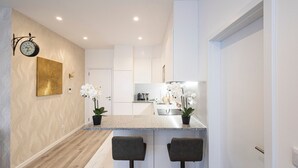 A modern kitchen with white cabinetry, a granite countertop, and two bar stools. - CasaBela 5 Star Matosinhos Sun&Beach by LovelyStay (Matosinhos)