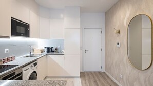 Cocina compacta con microondas, lavaplatos y lavadora, una puerta blanca y un espejo grande en la pared.