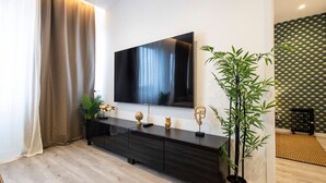 Una sala de estar moderna con un televisor de pantalla plana grande montado en la pared, un aparador de madera oscura con objetos decorativos y una planta de bambú grande.