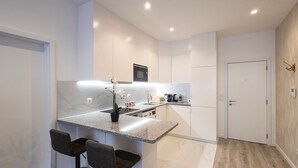 Una cocina moderna con encimera de mármol, horno integrado y cafetera. Hay dos taburetes de bar y una orquídea en maceta.