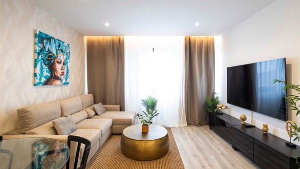 Una sala de estar moderna con un sofá color beige, una mesa redonda, un televisor y un cuadro en la pared.