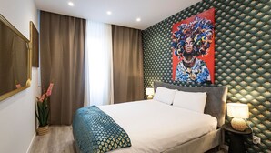 Habitación de hotel con una cama grande, un cuadro en la pared, una planta en maceta y una mesita de noche con una lámpara.