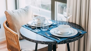 A dining table set with plates, bowls, cutlery, and wine glasses, positioned near a window with curtains.