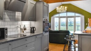 A modern kitchen with grey cabinets, a microwave, and a kettle. There is a bar stool and a large window with a view of the outdoors.