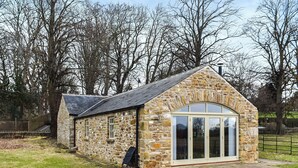 A stone cottage with a sloped roof, a large arched window, and a small porch area.