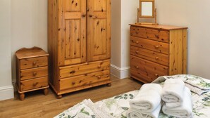 A bedroom with a wooden wardrobe, a smaller dresser, and a bed with a floral bedspread.