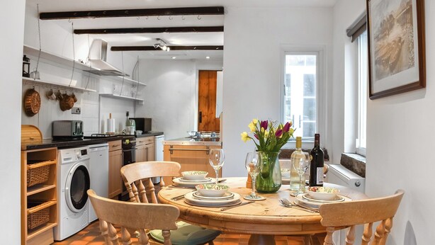 A dining area with a round wooden table, four chairs, and a vase with flowers. - 2 bedroom accommodation in Carnforth (Carnforth)