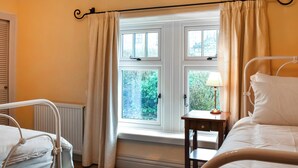 A bedroom with two beds, a window with curtains, a bedside table with a lamp, and a radiator. - 2 bedroom accommodation in Carnforth (Carnforth)