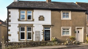 A two-story building with a white and brown facade, a stone foundation, and a black door. - 2 bedroom accommodation in Carnforth (Carnforth)