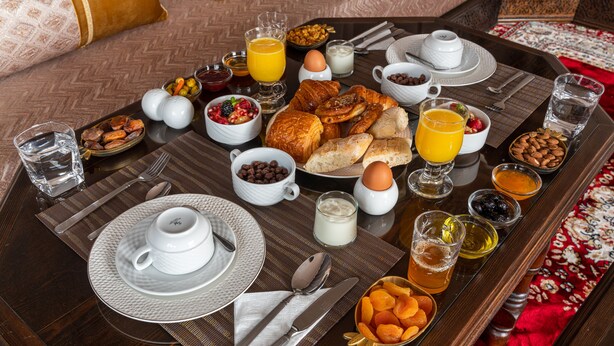 A breakfast tray with croissants, pastries, fruits, and beverages on a wooden table. - Yanis Guest House  (Marrakech)