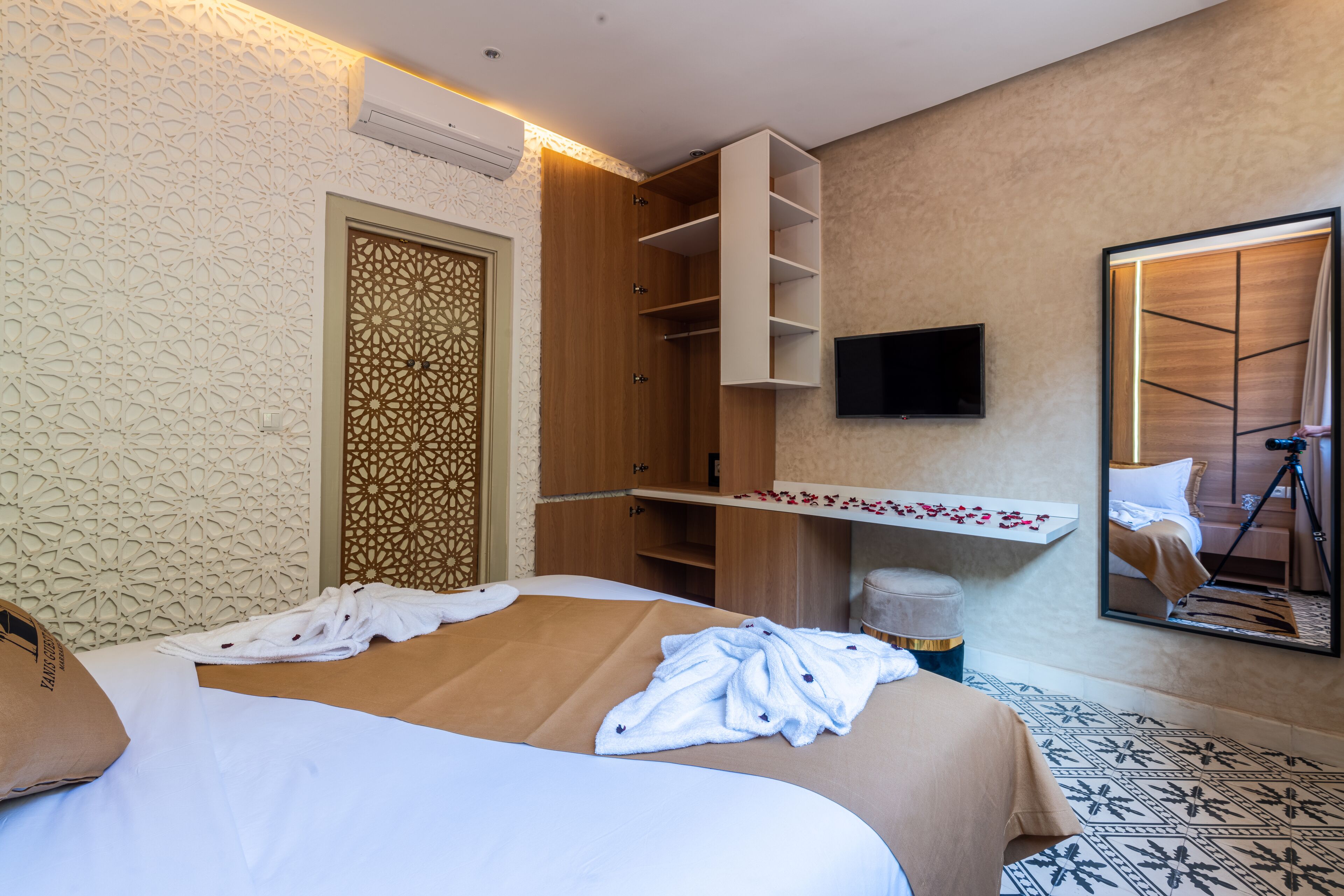 A hotel room with a large bed, a wooden wardrobe, a mounted TV, and a mirror reflecting the room.