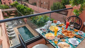 A balcony with a dining table set for breakfast, overlooking a swimming pool and lush greenery. - Yanis Guest House  (Marrakech)