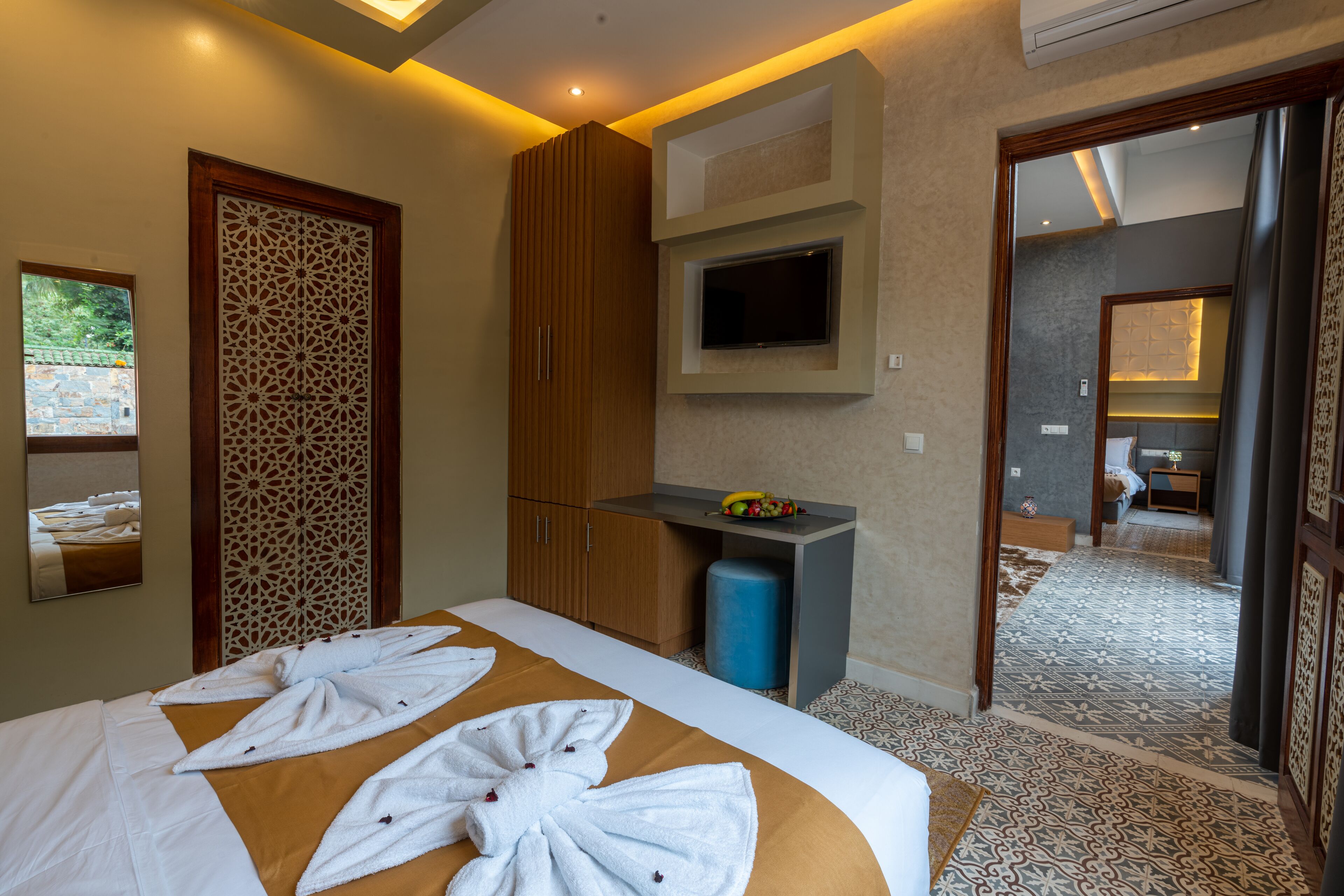A hotel room with a bed, a TV mounted on the wall, a small table with fruits, and a bathroom visible through an open door.