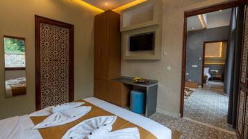 A hotel room with a bed, a TV mounted on the wall, a small table with fruits, and a bathroom visible through an open door.