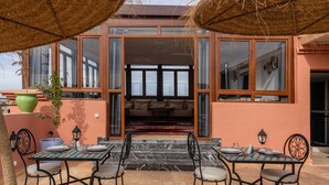 An outdoor dining area with a checkered table and chairs, a potted plant, and a view of the interior through glass doors. - Yanis Guest House  (Marrakech)