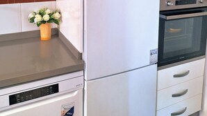 A kitchen with a white refrigerator, a microwave, and a built-in oven. There is a small flower vase on the countertop. - Feria Especial (Sevilla)