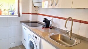 A compact kitchen with a washing machine, a built-in oven, a sink, and a window with potted plants. - Feria Especial (Sevilla)