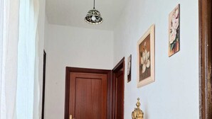 A hallway with a wooden door, a white console table with a decorative item, and two framed floral paintings on the wall. - Feria Especial (Sevilla)