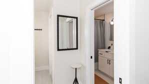 A hallway with a white door, a black-framed mirror, and a small white table. - The Inn at Fulton (Sandusky)