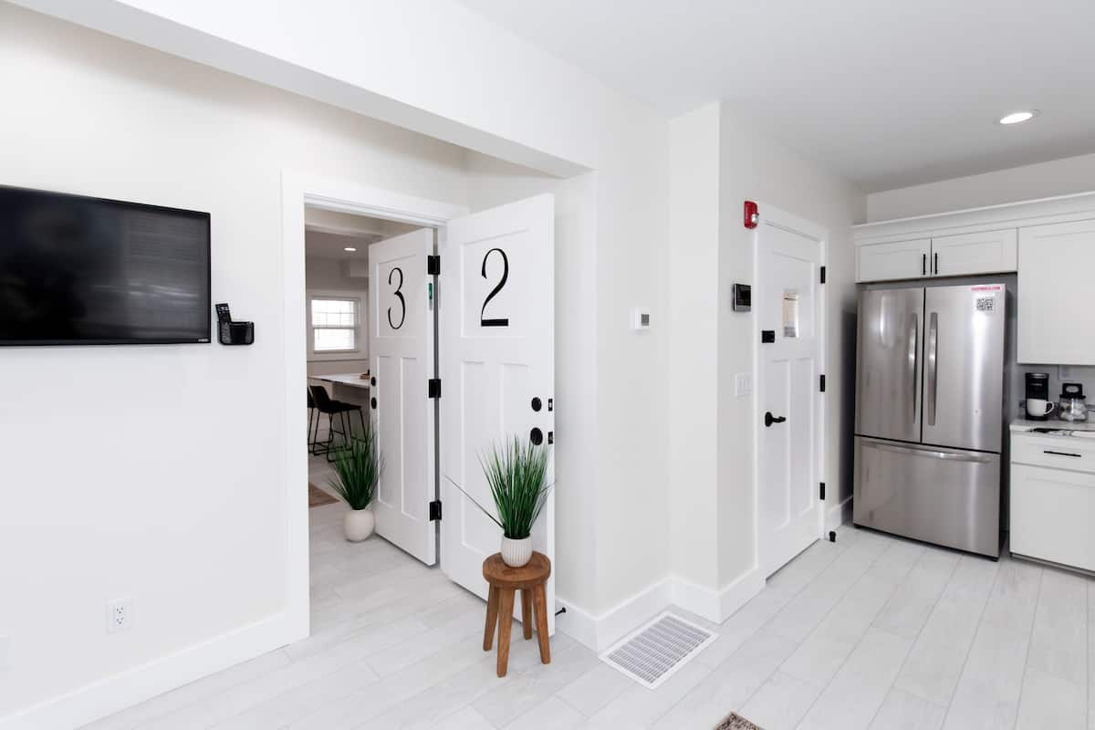 A modern kitchen with white cabinetry, a stainless steel refrigerator, and a potted plant on a wooden stool.