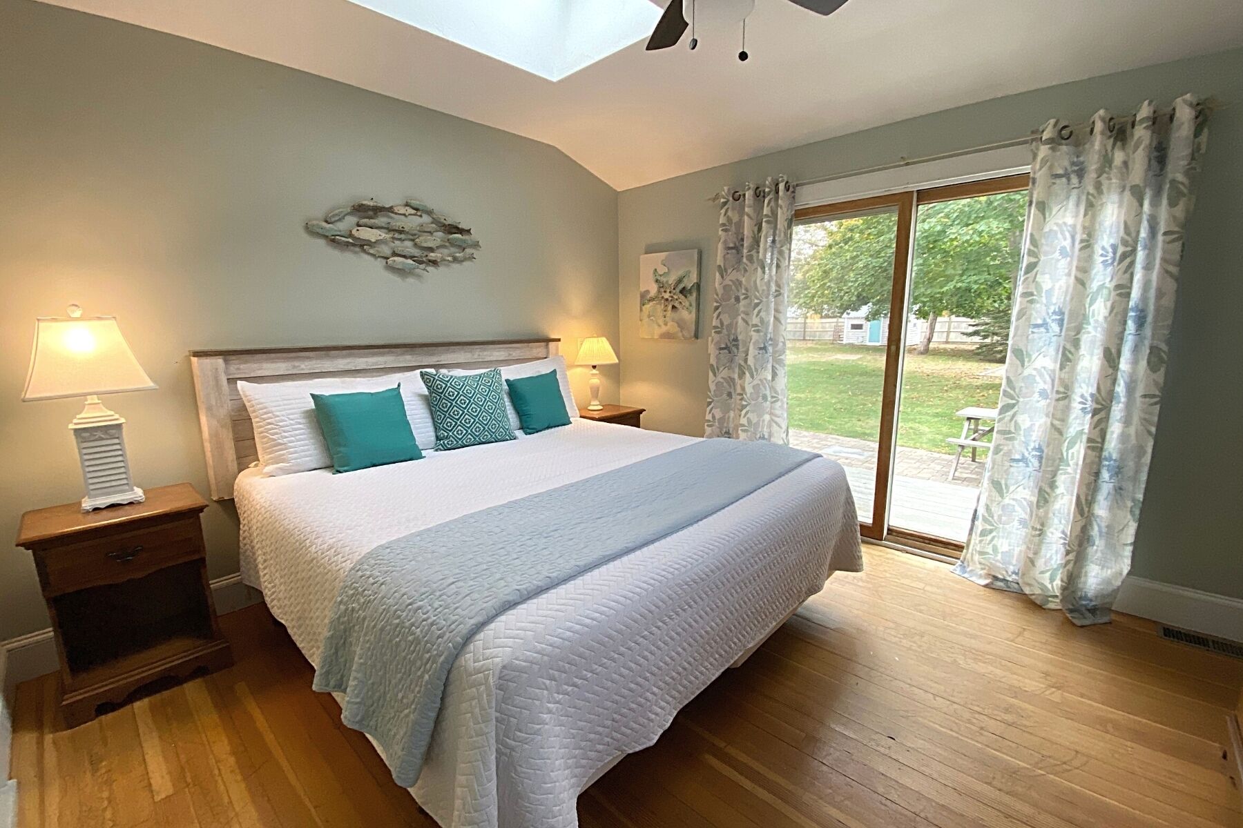 A bedroom with a large bed, two bedside tables, a ceiling fan, and a view of the outdoors through a sliding glass door.