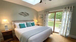 A bedroom with a large bed, two bedside tables, a ceiling fan, and a view of the outdoors through a sliding glass door.