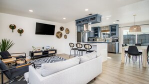 A modern living room with a sofa, a TV, and a dining area with chairs and a table.