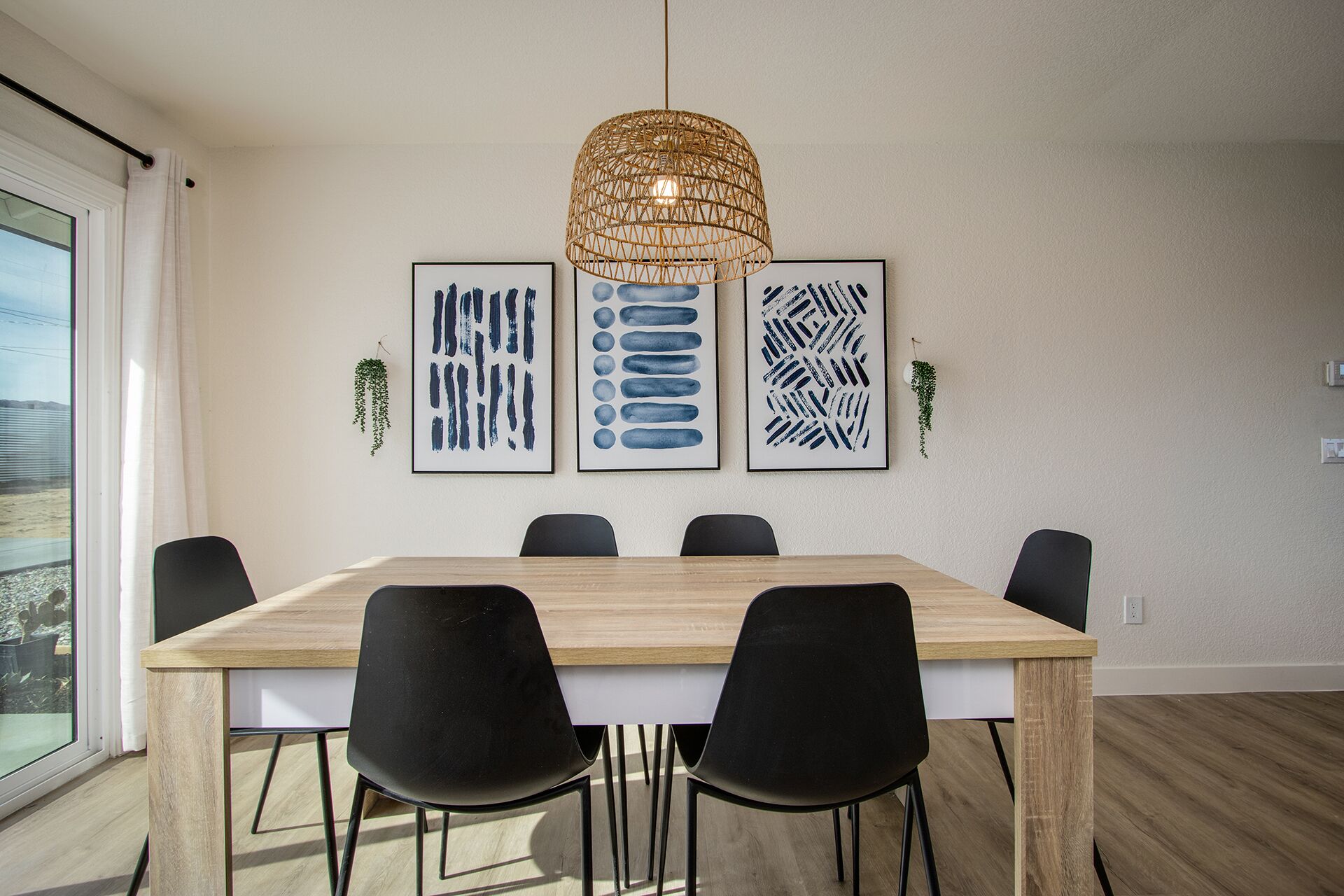 A dining area with a wooden table, black chairs, and three framed abstract artworks on the wall.